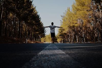 Man with arms outstretched walking on road amidst trees