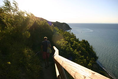 Man walking by railing at beach against clear sky