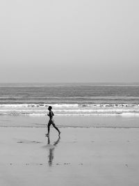 Side view of man running on shore against clear sky