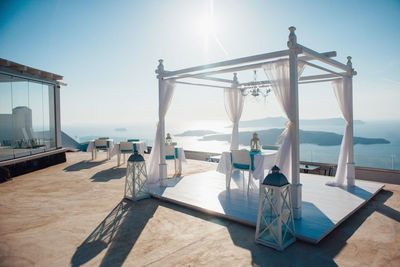 Chairs by swimming pool by sea against sky on sunny day