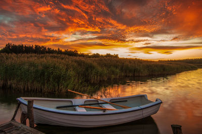 Boat moored in lake against sky during sunset