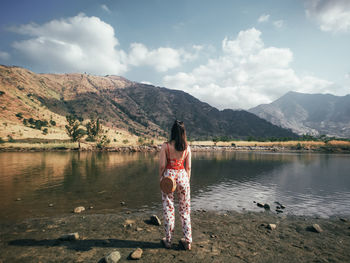 Rear view of woman standing at lakeshore against mountains