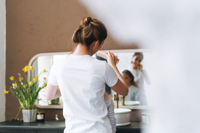 Young mother woman with little girl daughter in pajamas combs hair on morning in bathroom at home