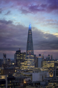 Illuminated buildings in city against cloudy sky