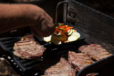 Cropped image of hand preparing meat on barbecue grill