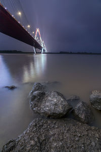 Illuminated bridge over sea against sky at night