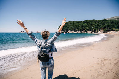 Rear view of person standing at beach against sky