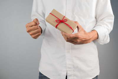 Midsection of man holding paper while standing against white background