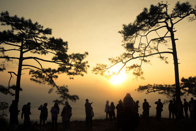 Silhouette people by trees against sky during sunset