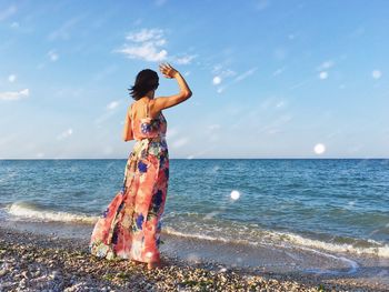 Rear view of woman standing on shore at beach against sky