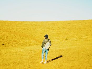 Rear view of woman standing on yellow field during sunny day