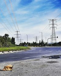 Road by electricity pylon against sky