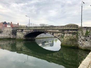 Arch bridge over river by buildings against sky