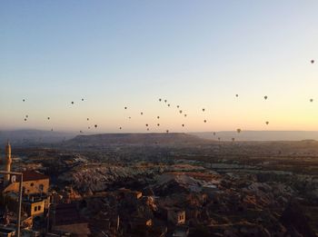 Hot air balloons flying over landscape against clear sky during sunset