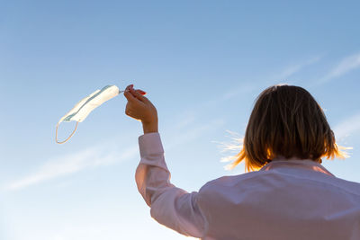 Low angle view of woman holding mask against sky