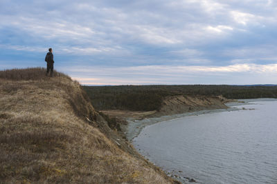 Man standing on cliff by sea against sky