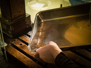 Cropped hands of person emptying water from tray into wooden crate