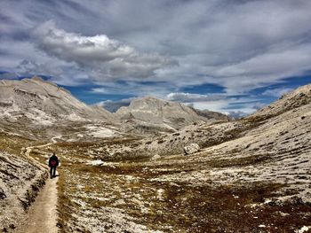 Man walking on mountain trail against sky