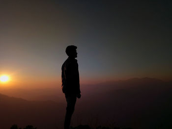 Silhouette man standing on mountain against clear sky during sunset