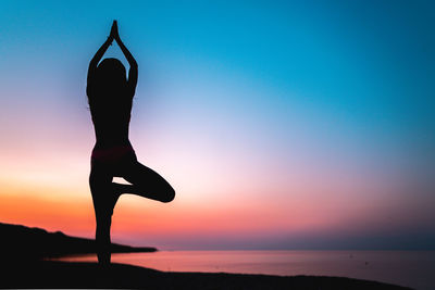 Silhouette woman with arms raised against sky during sunset