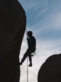 Low angle view of silhouette man climbing rock against sky