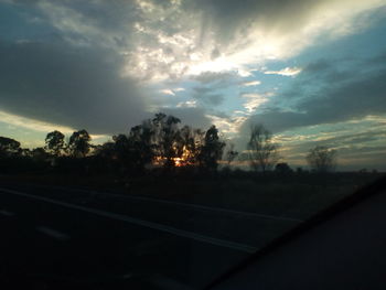 Silhouette trees by road against sky during sunset