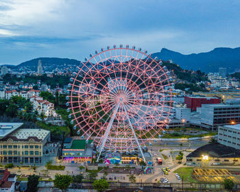 Illuminated ferris wheel in city against sky