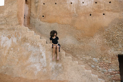 Woman sitting on staircase against building in city