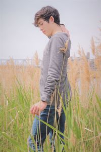 Young man looking in field of long grass against sky