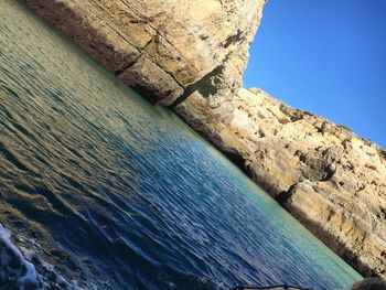 Low angle view of rock formation by sea against clear blue sky