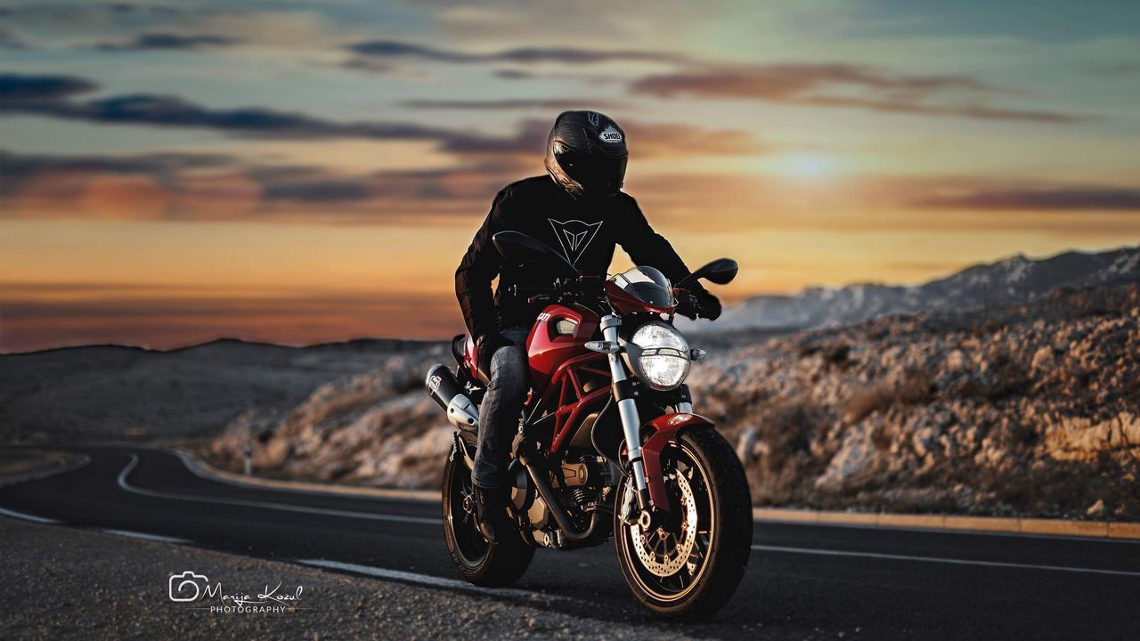 MAN RIDING MOTORCYCLE ON ROAD AT SUNSET