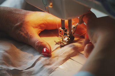 Photo of woman's hands with red nail polish in process of sewing linen dress using sewing machine 