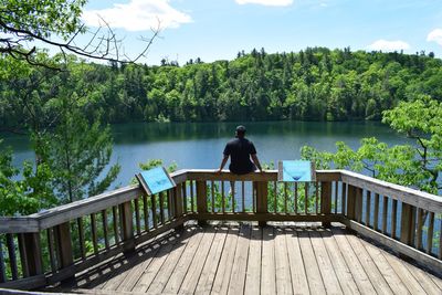 Rear view of man sitting on railing by lake