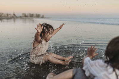 Rear view of mother and daughter at shore against sky during sunset