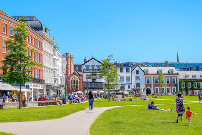 People in park by buildings against clear blue sky