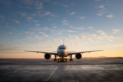 Airplane on runway against sky during sunset