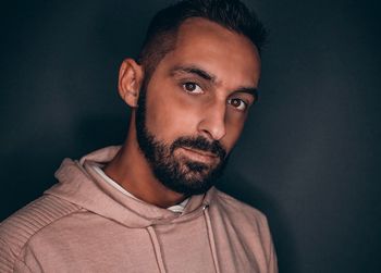 Portrait of bearded young man standing against black background