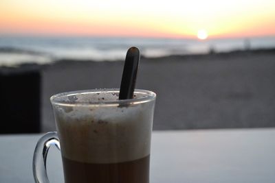 Close-up of coffee cup on table against sea during sunset