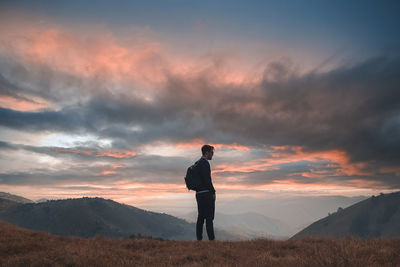 Rear view of man standing on land against sky during sunset