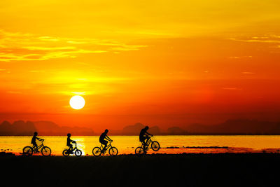 Silhouette boys riding bicycle against orange sky
