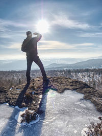 Standing man with raised arm on icy stone and looking on snow covered mountains. landscape traveler
