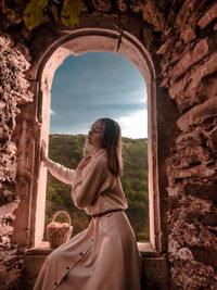 Side view of woman sitting against stone wall