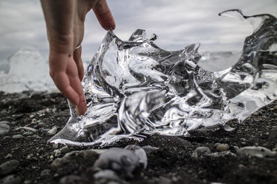 Cropped hand of woman touching ice on black sand at beach