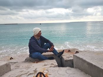 Man sitting at beach against sky