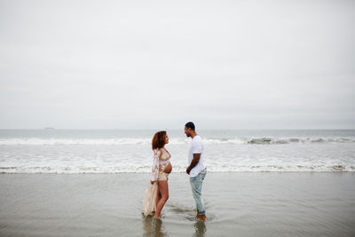 Mixed race couple posing on beach, maternity