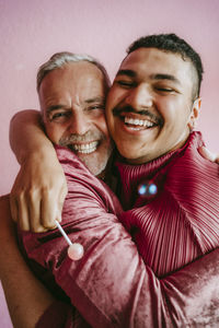 Happy gay friends embracing each other against wall at home