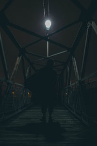 Rear view of person walking on illuminated footbridge