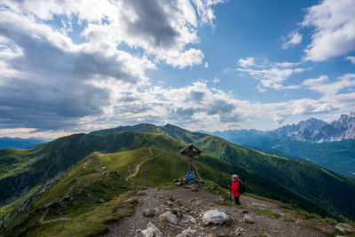 Hiker looking at cross on mountain against sky