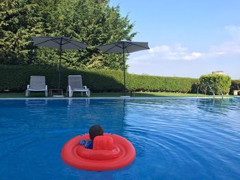 Rear view of boy wearing inflatable ring swimming on pool against sky