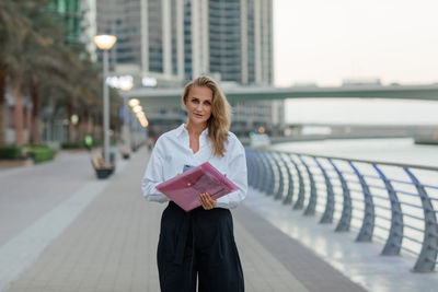 A beautiful business woman with a folder of documents in her hands outdoors. city portrait